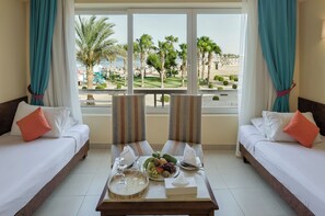 A hotel room with two beds, a dining table with fruit and glasses, and a view of a beach and palm trees. - Shoni Bay Resort (Marsa Alam)