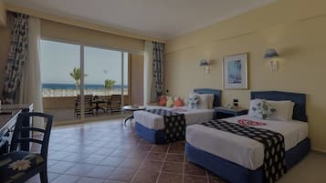 A hotel room with two beds, a balcony with a view of the sea, and a dining area with chairs and a table.