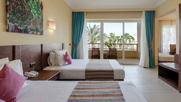 A hotel room with two beds, a painting on the wall, a balcony with chairs, and a view of palm trees.