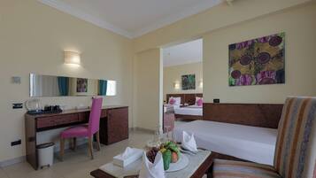 Habitación de hotel con cama, escritorio, silla, una pequeña mesa con frutero y un cuadro en la pared.