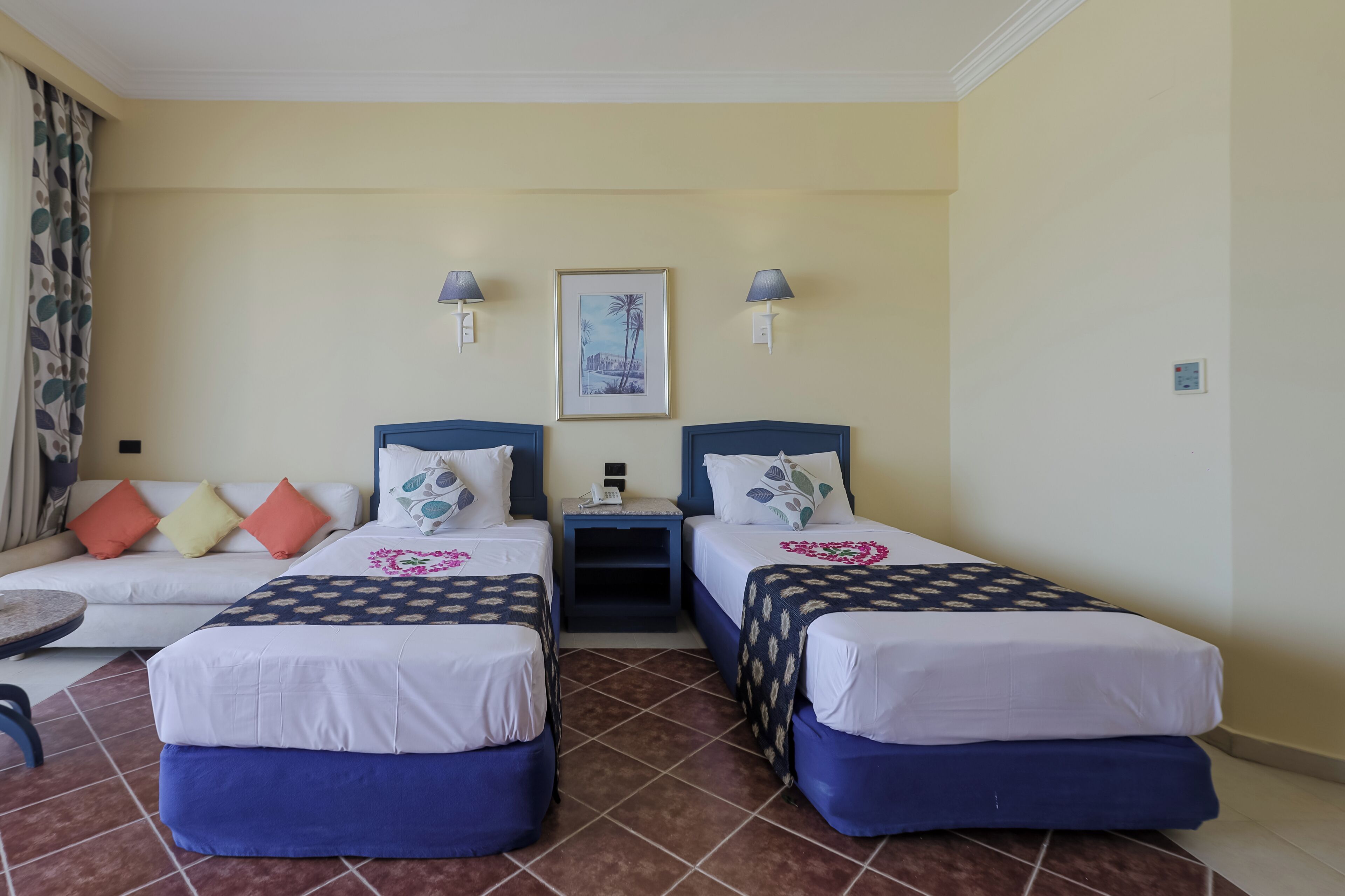 A hotel room with two beds, a sofa, a small table, and a picture on the wall.