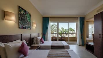 Habitación de hotel con dos camas, un cuadro grande, un balcón con vistas a palmeras y una puerta corredera.