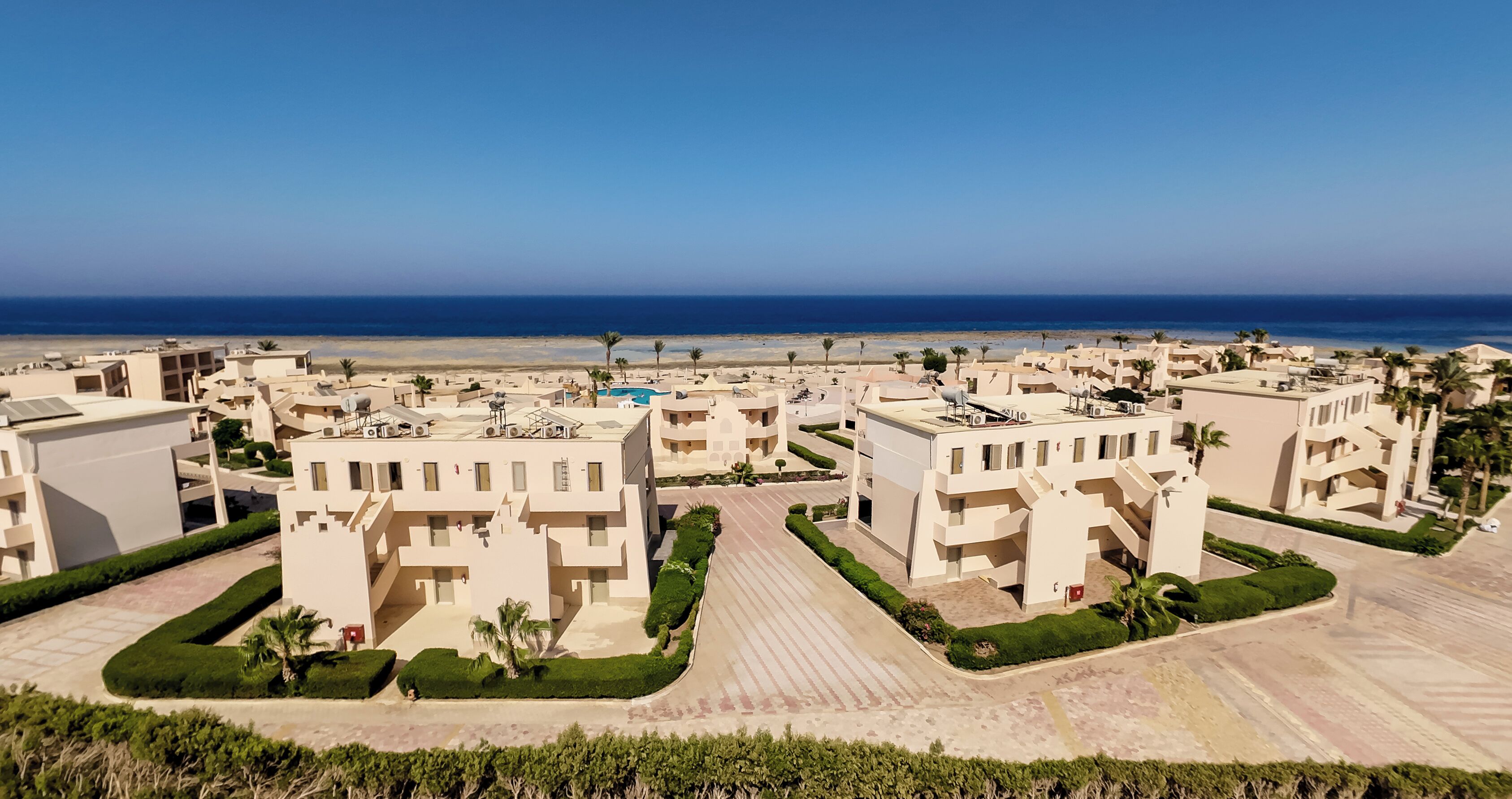 Un complejo turístico costero con arquitectura moderna, una piscina central y vistas a la playa.