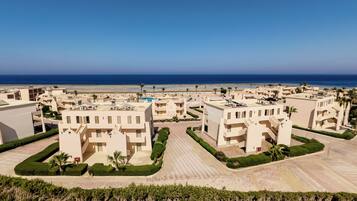 Un complejo turístico costero con arquitectura moderna, una piscina central y vistas a la playa.