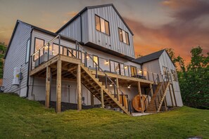 A two-story house with a wooden deck and stairs leading to the upper level. - Luxury Trail Home W Sauna, Hot tub, Steam shower (Bella Vista)