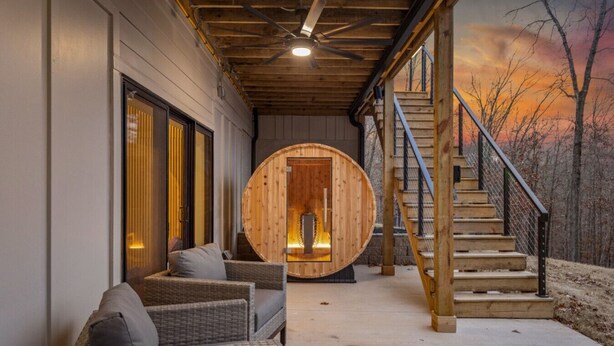 A wooden sauna with a circular door, wicker chairs, and a staircase leading to a deck. - Luxury Home on trail W Sauna/Hot tub/Steam room (Bella Vista)