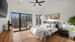 A spacious bedroom with a large bed, a ceiling fan, a sliding glass door leading to a balcony, and a painting on the wall. - Luxury Home on trail W Sauna/Hot tub/Steam room (Bella Vista)