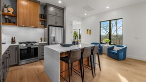 A modern kitchen with a central island, bar stools, and a seating area with blue chairs. - Luxury Home on trail W Sauna/Hot tub/Steam room (Bella Vista)