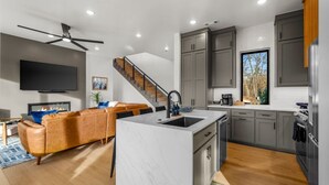 A modern kitchen with a central island, grey cabinets, and a large window.