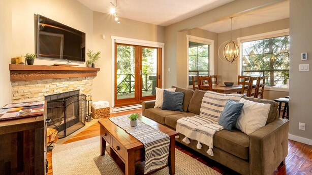 A spacious living room with a fireplace, a sofa, a coffee table, and a dining area with chairs and a table. - Crystal Ridge by Whistler Retreats (Whistler)