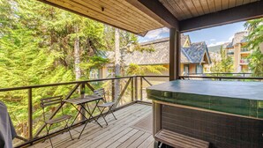 A wooden deck with a hot tub, outdoor seating, and a view of a forested area. - Crystal Ridge by Whistler Retreats (Whistler)