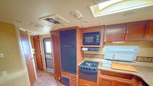 A compact RV kitchen with a microwave, stove, and sink. - Crazy Mountain Camper NE of Livingston (Livingston)