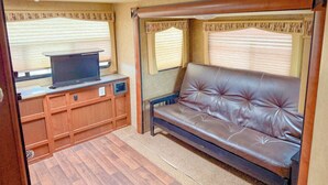 A compact RV interior with a wooden entertainment unit, a leather couch, and a small TV. - Crazy Mountain Camper NE of Livingston (Livingston)