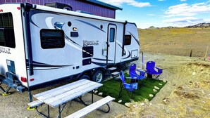 A Kodiak RV parked next to a building with a picnic table and blue chairs. - Crazy Mountain Camper NE of Livingston (Livingston)