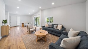 A spacious living area with a grey sofa, a round wooden coffee table, and a dining table with chairs.