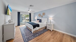 A bedroom with a bed, bedside tables, a ceiling fan, and a view of the outdoors.