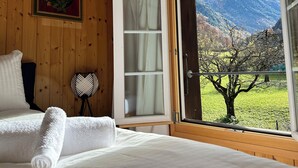 Un dormitorio con pared de paneles de madera, una cama con ropa blanca, una ventana con vistas a montañas y un cuadro enmarcado sobre la cama.