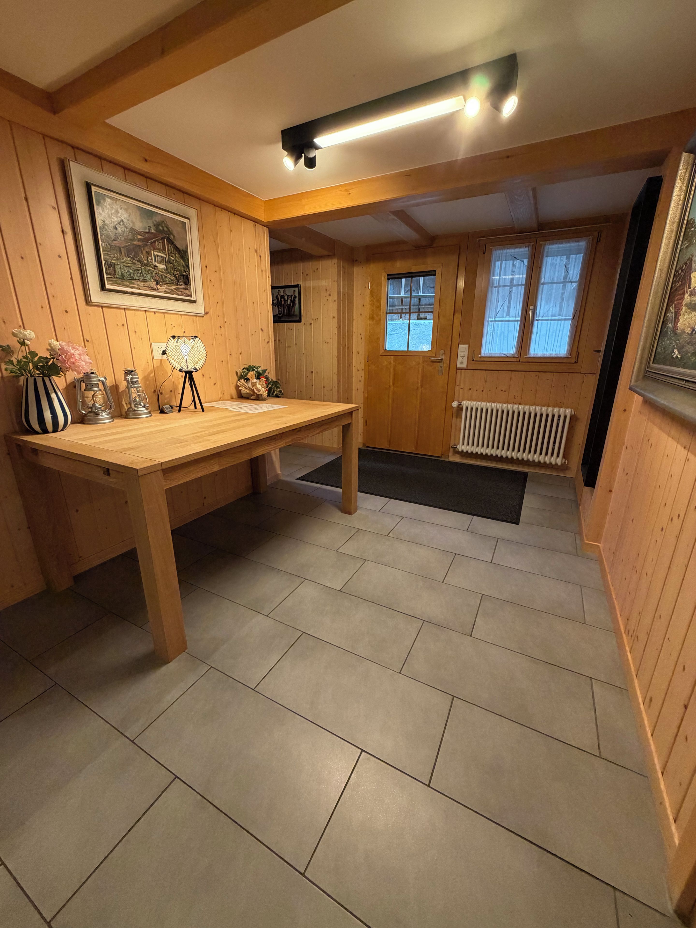 A wooden interior with a table, framed pictures, and a radiator.