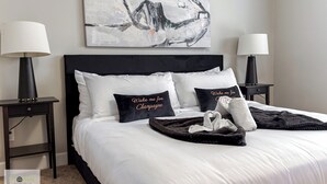 A neatly made bed with white linens, two black nightstands with lamps, a black headboard, and two pillows with text. - Luxury Executive 4BD 2.5B AC home in the exclusive neighbourhood of Windermere (Edmonton)