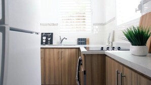Een moderne keuken met houten kastjes, een wit aanrecht, een spoelbak en een plant in pot.
