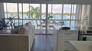 En moderne stue med udsigt over lystbådehavnen, en sofa, spiseområde og køkken.
