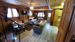 L’intérieur chaleureux d’un chalet avec un plancher en bois, un canapé, une table à manger et un téléviseur fixé au mur.