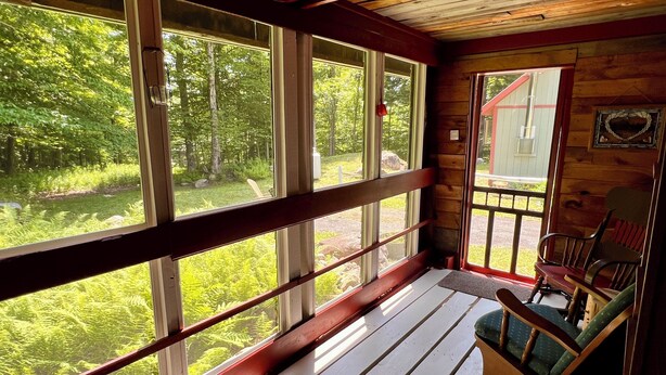 Une cabane en bois dotée d’une véranda, de grandes fenêtres et offrant une vue sur la forêt.