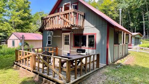 Une cabane en bois dotée d’une terrasse, d’un barbecue et d’un petit porche.