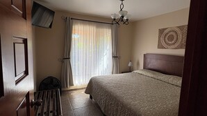 A bedroom with a bed, a chair, a TV mounted on the wall, a ceiling fan, and a window with curtains. - Villas San Francisco (Huichapan)