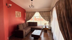 A living room with a sectional sofa, a coffee table, a wall-mounted light fixture, and a window with curtains. - Villas San Francisco (Huichapan)