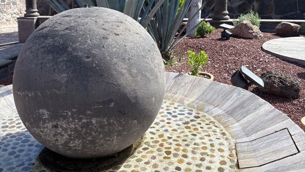 A stone sphere on a mosaic-tiled platform, surrounded by a stone wall and a tree. - Villas San Francisco (Huichapan)