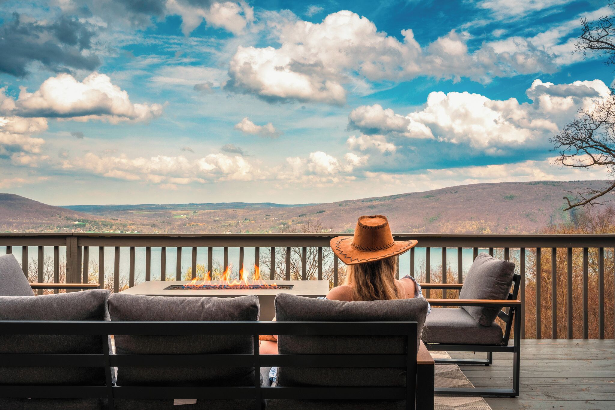 A deck with outdoor seating and a fire feature, overlooking a hilly landscape.