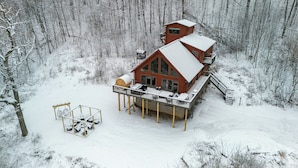 Una cabaña con terraza y una zona de estar cubierta al aire libre, rodeada por un bosque nevado.