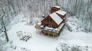 Une cabane dotée d’une terrasse et d’un espace extérieur aménagé et abrité, entourée d’une forêt enneigée.