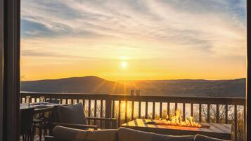 A sunset view from a balcony with a fire feature, outdoor seating, and a table.