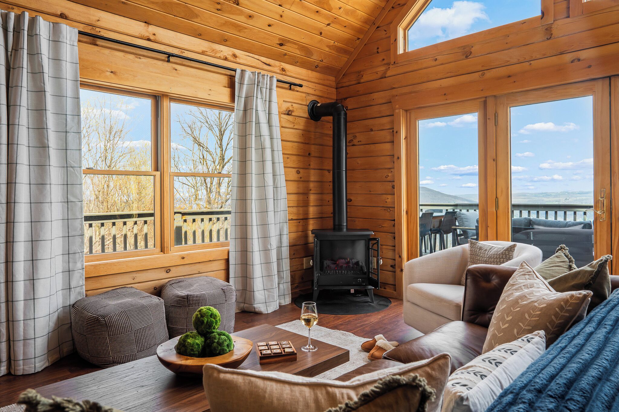 A cozy cabin interior with a fireplace, wooden walls, and a view of the outdoors.