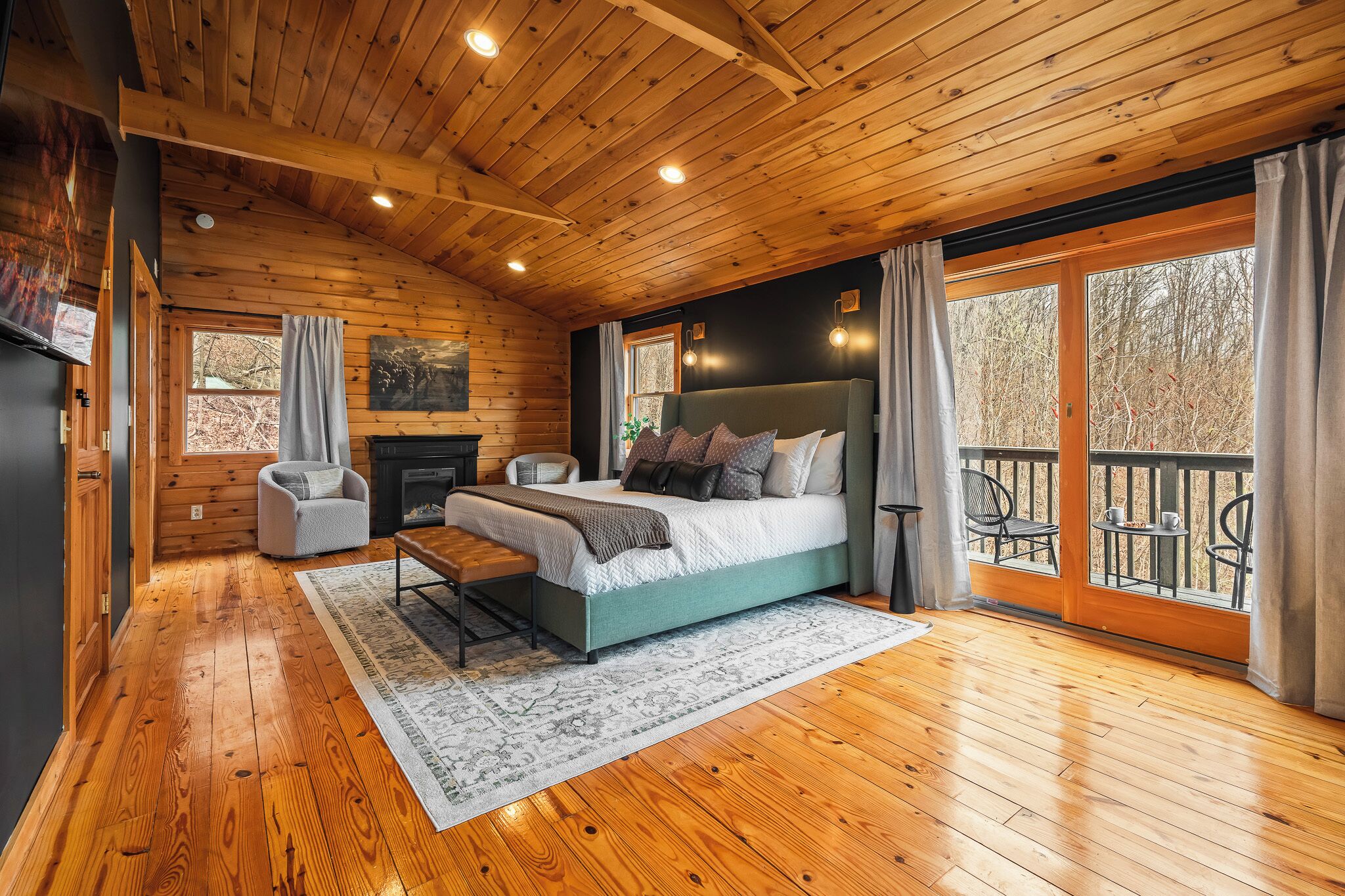 A wooden cabin interior with a bed, seating area, fireplace, and a balcony with a railing.