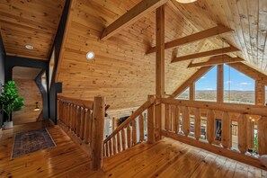 A wooden interior with a high ceiling, a staircase, and a large window offering a view of the landscape.