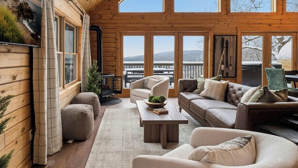 Interior acogedor de una cabaña con paredes de madera, un ventanal grande con vistas a un paisaje nevado, chimenea y asientos cómodos.