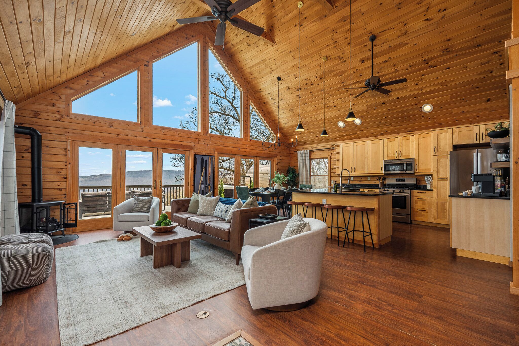 A spacious living area with a wooden ceiling, large windows, a fireplace, and a kitchen with modern appliances.