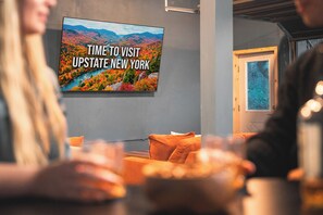 A room with a television displaying 'TIME TO VISIT UPSTATE NEW YORK' and a view of a mountainous landscape.