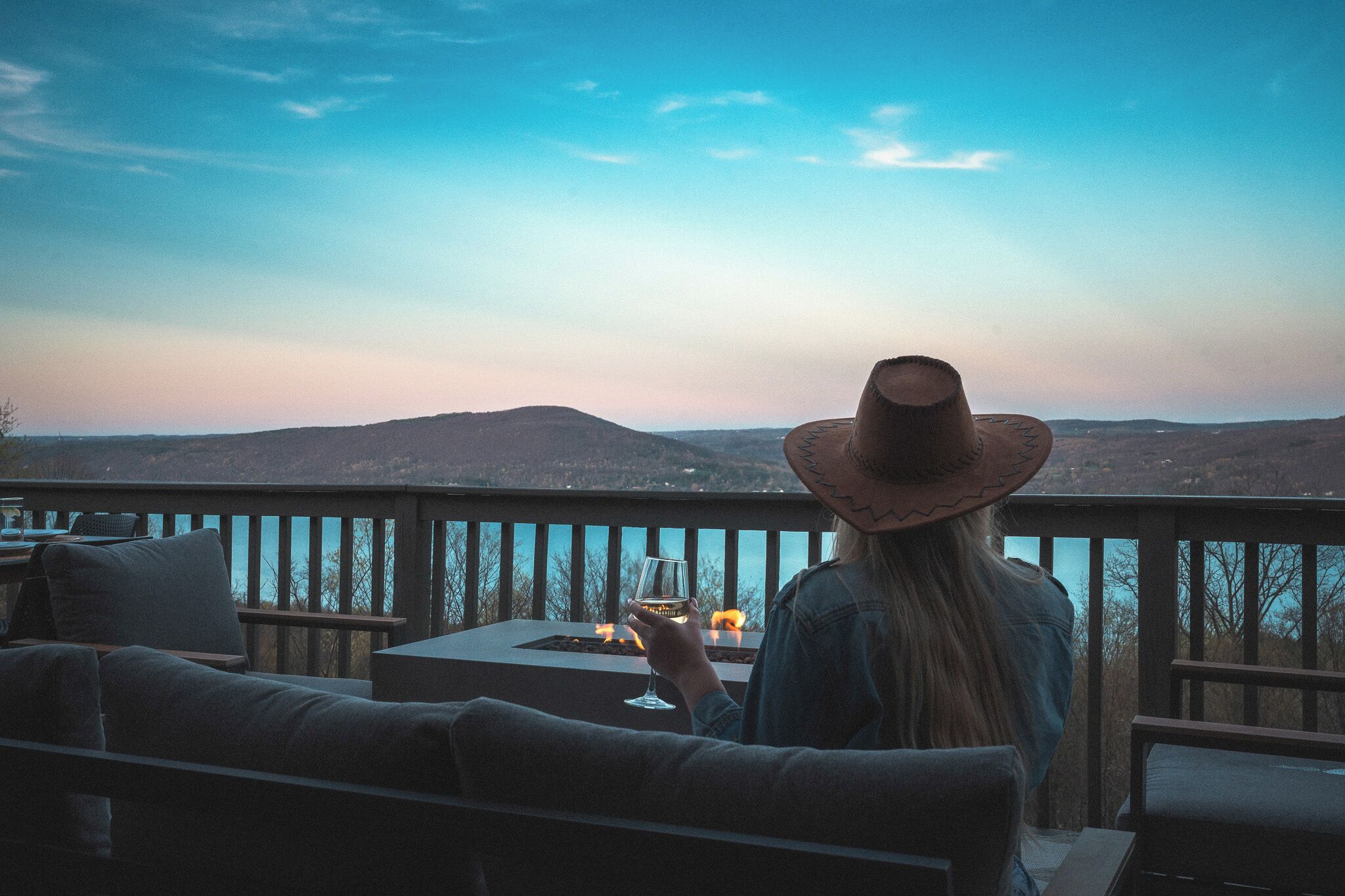 A person seated on a deck chair with a view of a mountainous landscape.