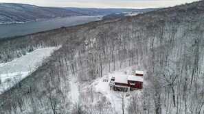 A cabin with a snow-covered roof, surrounded by a forested area with a lake in the background.