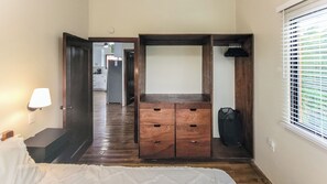 Ein Schlafzimmer mit Holzschrank, Bett, Nachttisch, Lampe und einem Fenster mit Jalousien.