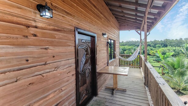 A wooden cabin with a balcony, a door with a bird design, and a view of lush greenery.