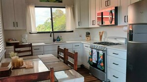 A compact kitchen with white cabinets, a gas stove, a built-in oven, a refrigerator, and a window with a view of greenery.