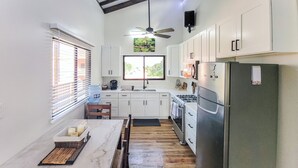 A compact kitchen with white cabinets, a stainless steel refrigerator, a stove, and a ceiling fan.