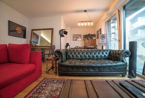 Ein Wohnzimmer mit einem roten Sofa, einem schwarzen Ledersessel, einem gemusterten Teppich und einem 'No Parking'-Schild.