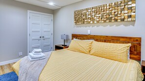 A bedroom with a large bed, a wooden headboard, a wall-mounted artwork, a bedside table with a lamp, and a door with a towel stack. - Luxury, well stocked Murray apartment. (Murray)