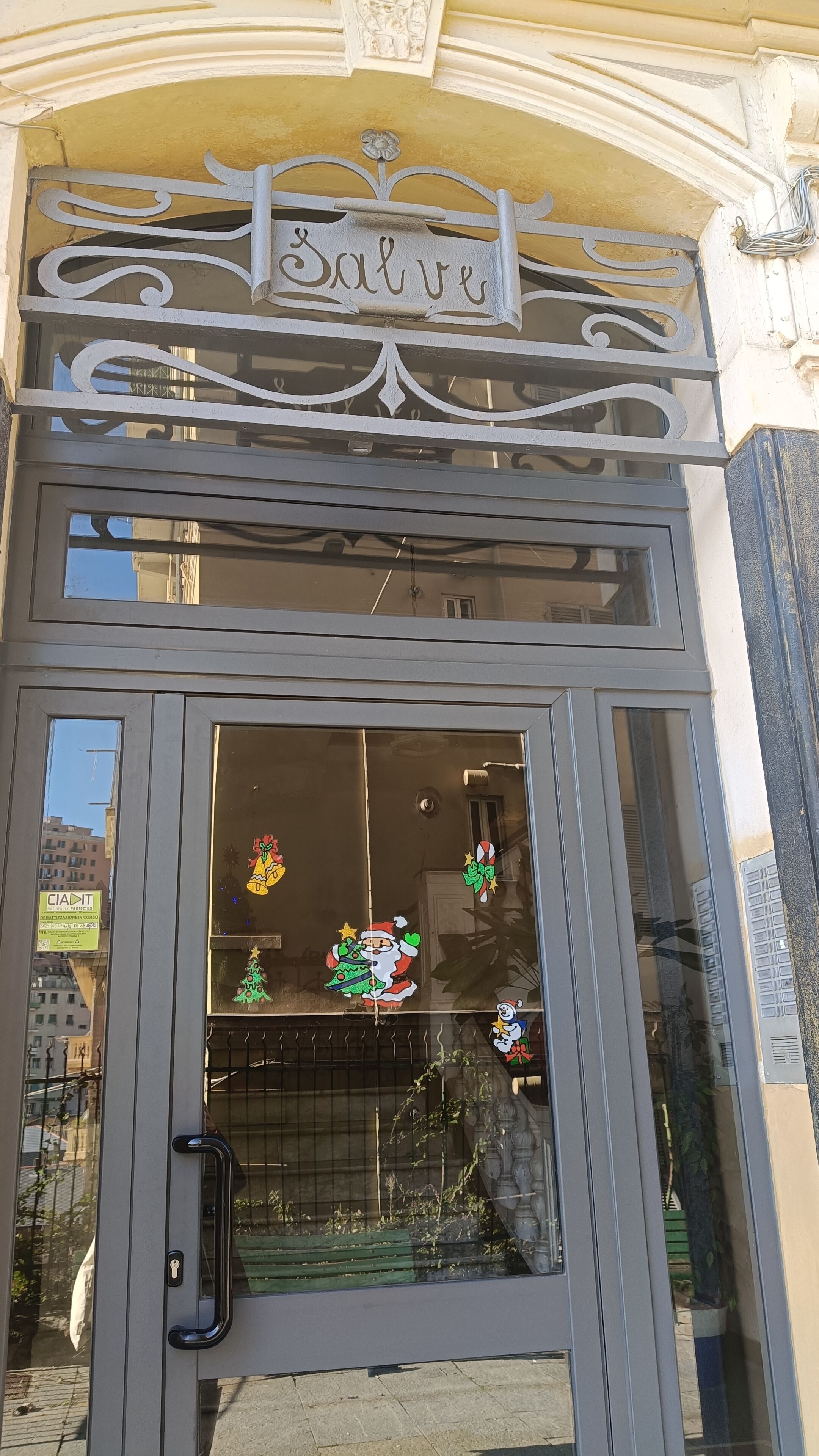Ein Gebäudeeingang mit einem Metallschild über der Tür, einem Fenster mit Weihnachtsdekoration und einem Schlüsselloch in der Tür.